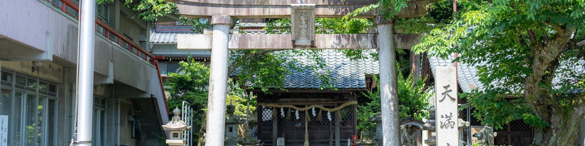 A traditional Japanese torii gate with a shrine in the background, surrounded by lush greenery and a stone monument with Japanese characters.