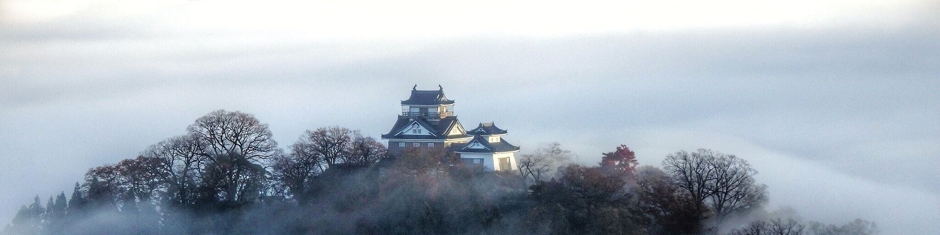 Um castelo japonês tradicional rodeado de árvores e envolvido em névoa.