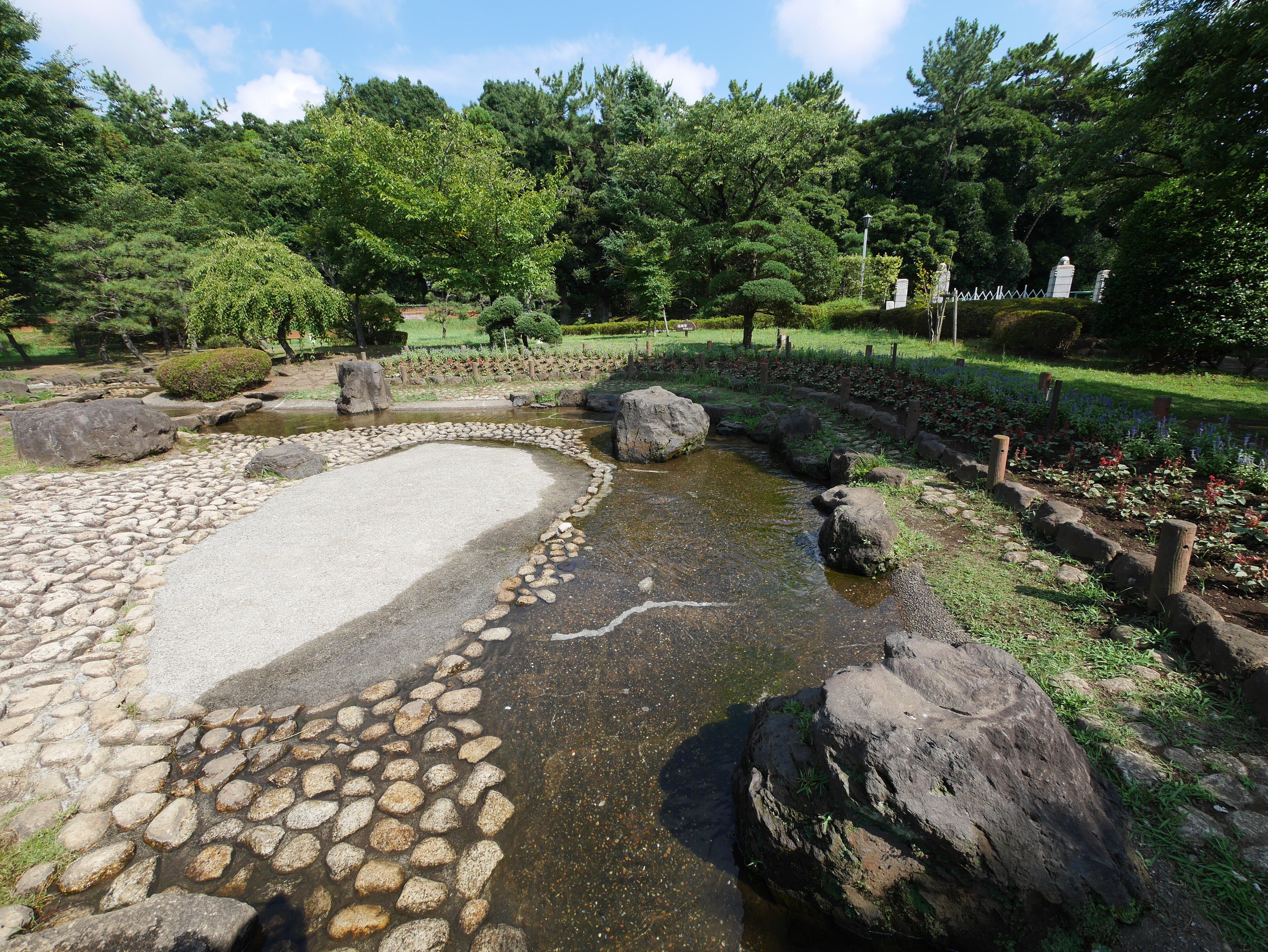 A serene garden with a pond, surrounded by rocks and lush greenery.