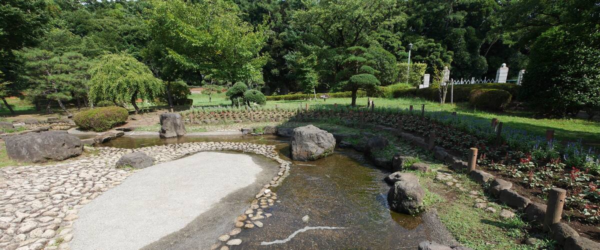 A serene garden with a pond, surrounded by rocks and lush greenery.