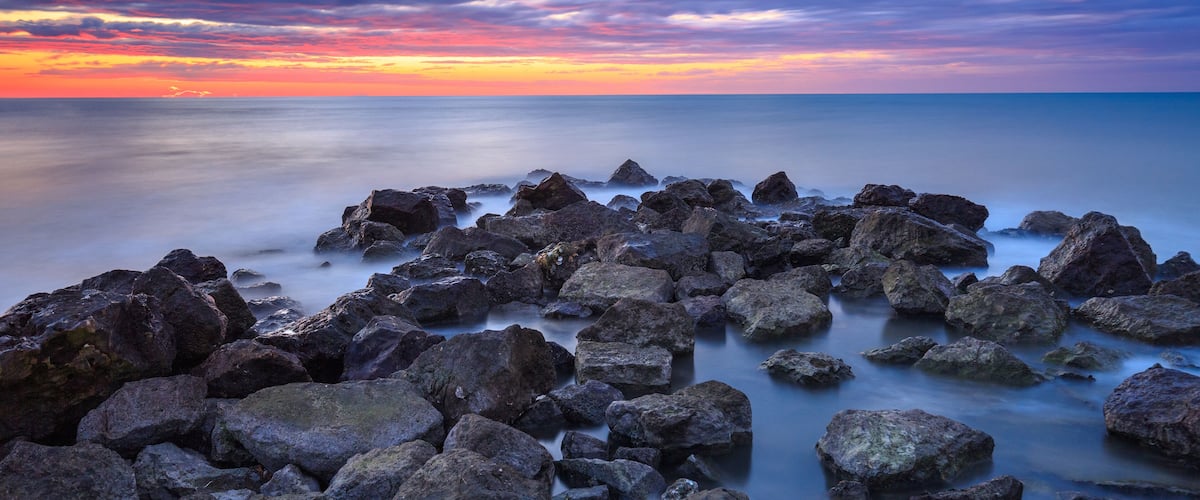 A rocky shoreline at sunset with a colorful sky.