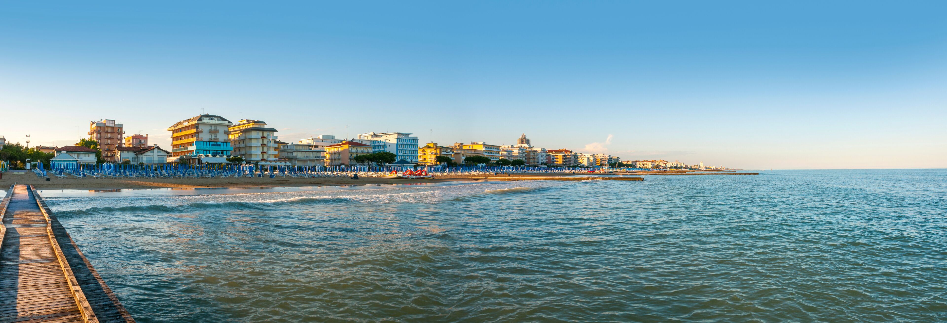 A coastal cityscape with a pier extending into the sea, colorful buildings, and a clear sky.