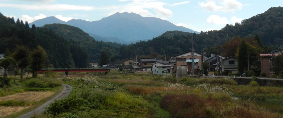 A rural landscape with a winding road, a small body of water, and houses in the foreground.