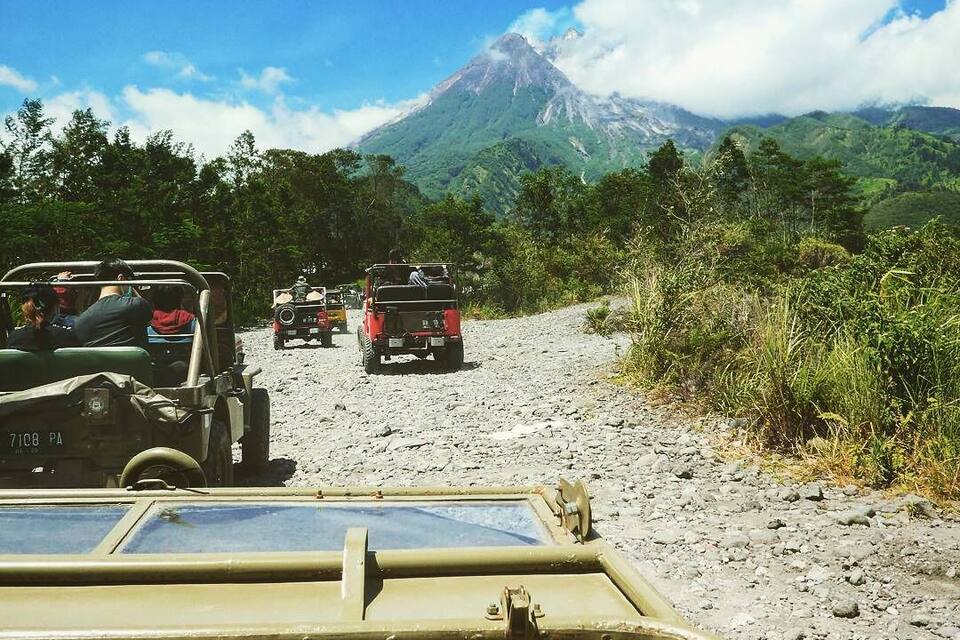 A convoy of off-road vehicles on a dirt road with a volcano in the background.