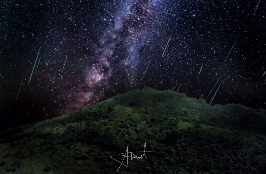A starry night sky over a grassy hill.
