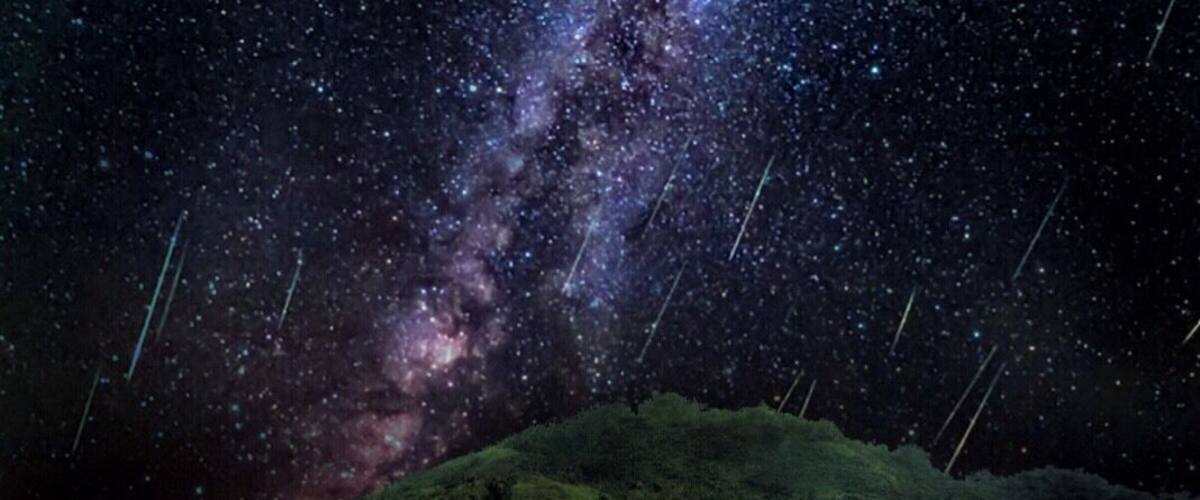 A starry night sky over a grassy hill.