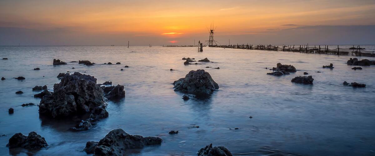 A rocky shoreline at sunset with a pier extending into the water.