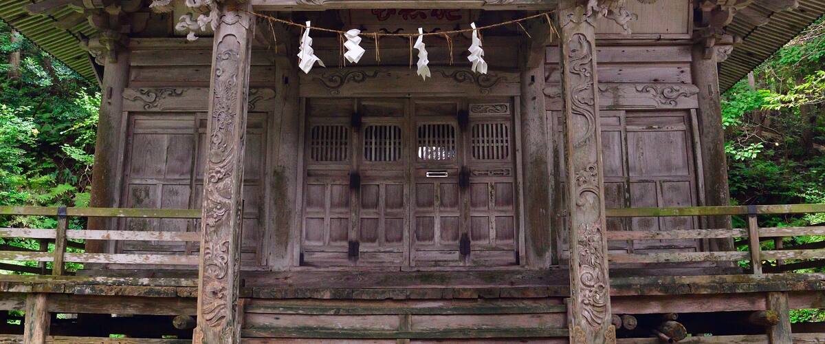 A traditional wooden shrine with ornate carvings and a tiled roof, surrounded by lush greenery.