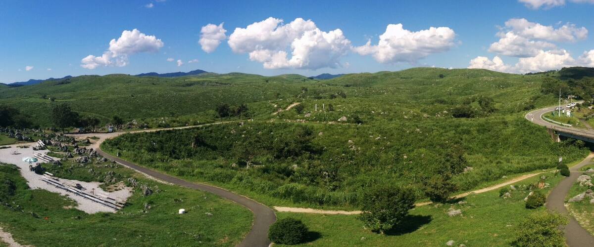 A green valley with a winding road, a bridge, and distant mountains.