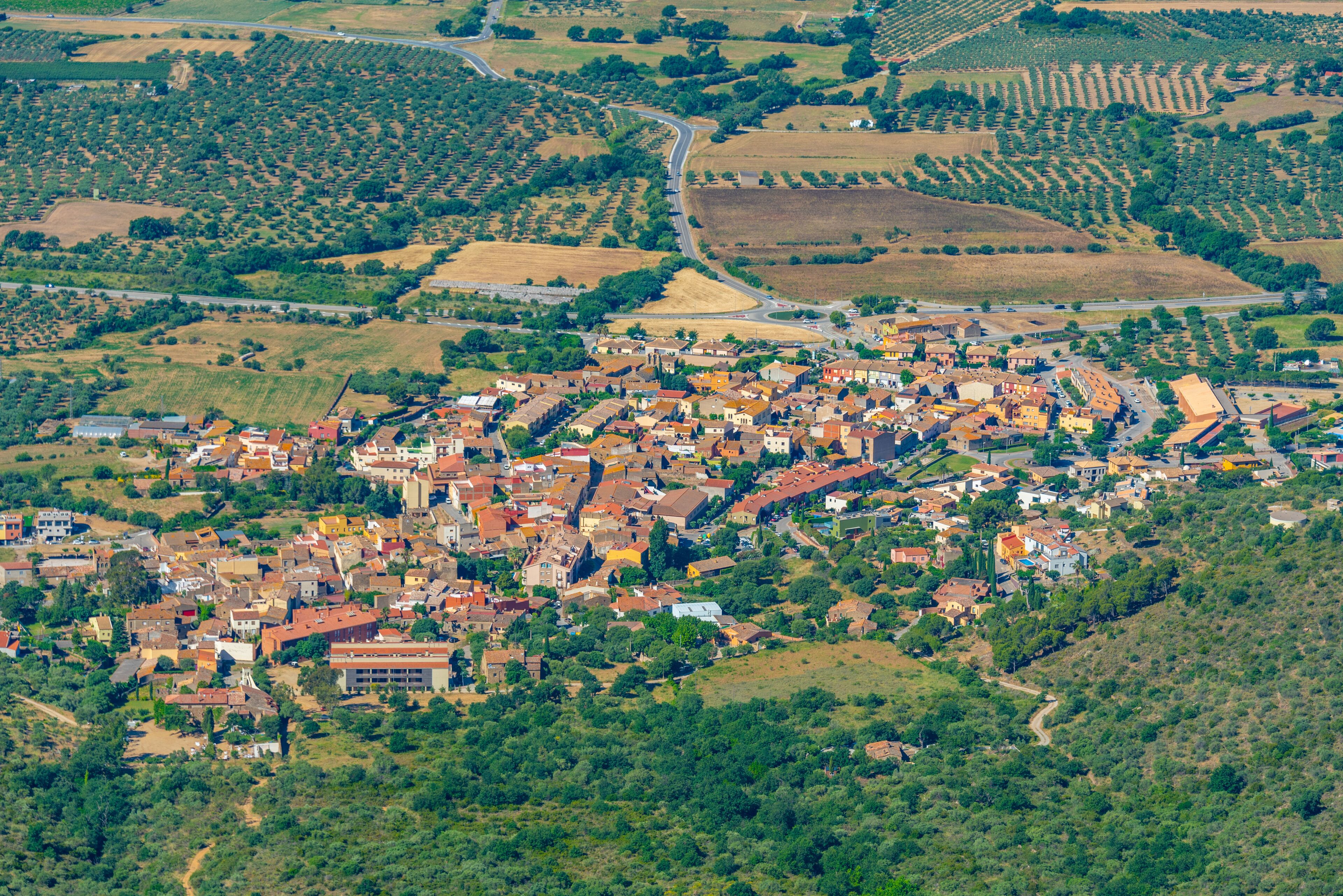 An aerial view of a town with a dense cluster of buildings, surrounded by agricultural fields and rolling hills.