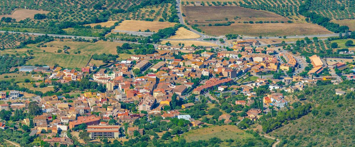 An aerial view of a town with a dense cluster of buildings, surrounded by agricultural fields and rolling hills.
