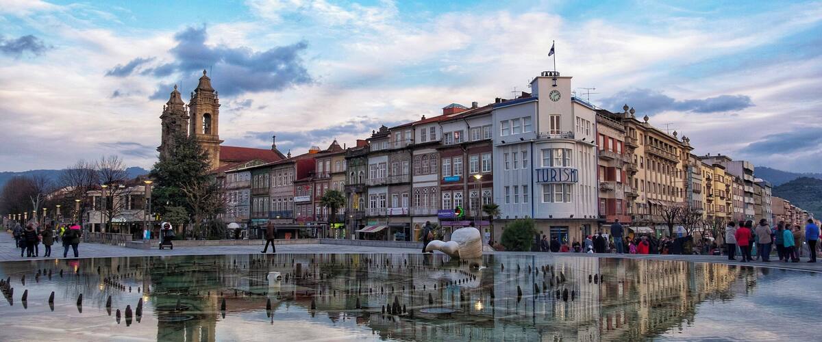 A historic town square with a central fountain reflecting buildings and a prominent clock tower.