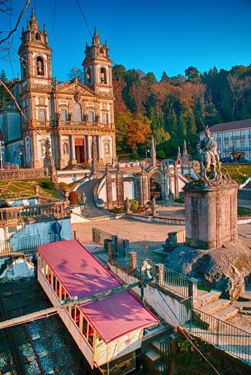 A historic church with two towers, a statue, and a red-roofed building.