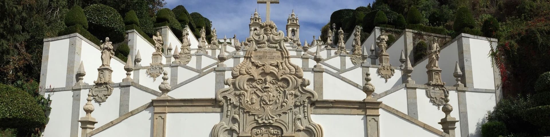 A white ornate gate with a fountain in the center, surrounded by steps and statues.