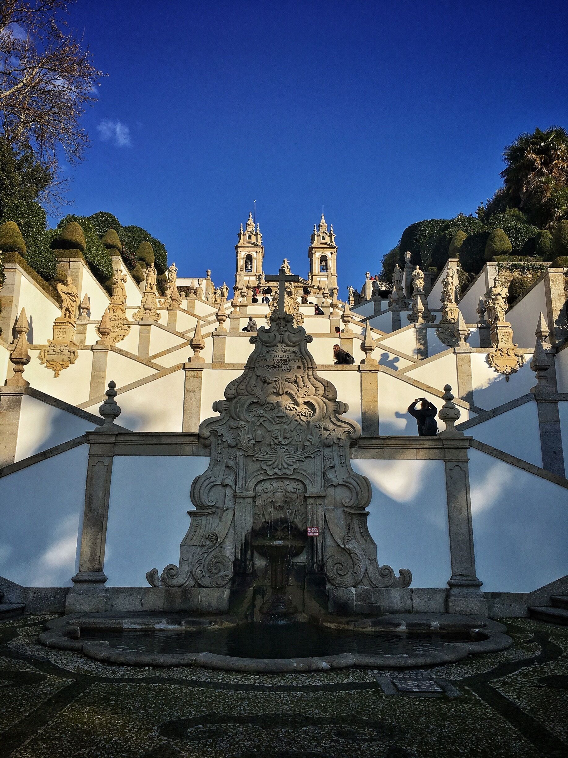 A grand staircase leading to a historic church with ornate statues and a fountain at the base.