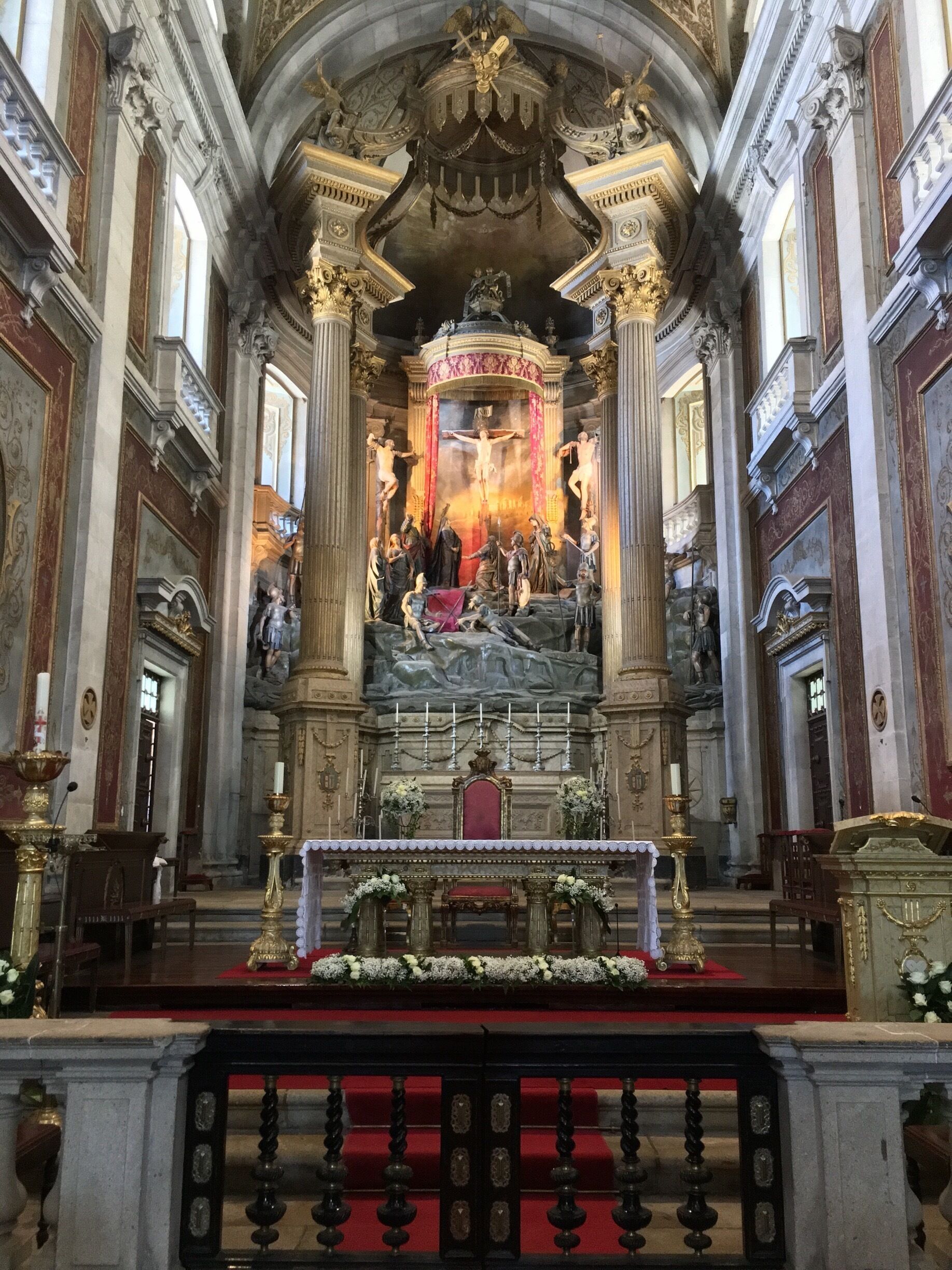 Interior de igreja ornamentado com cena central da crucificação, colunas e decorações florais.