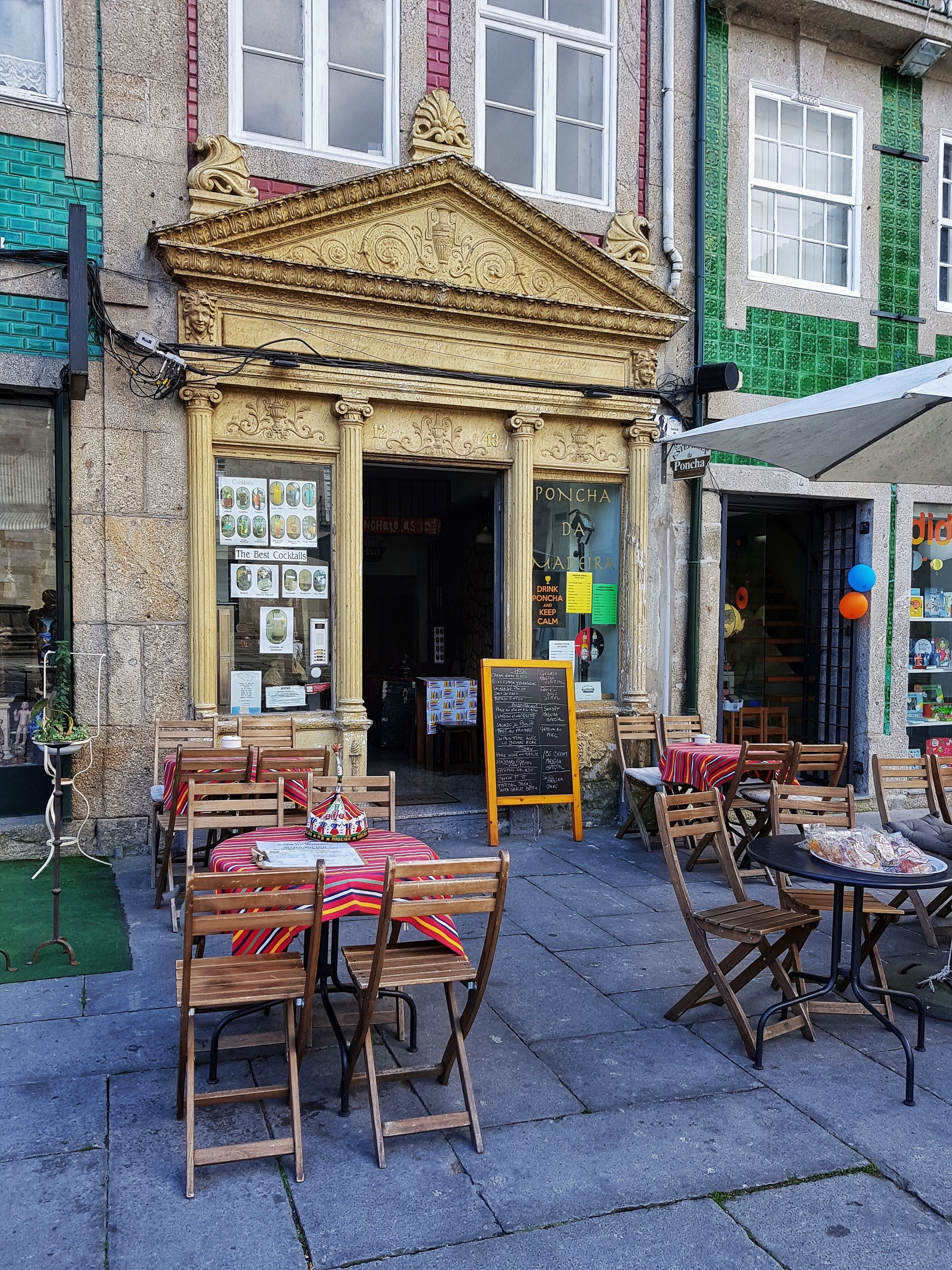 Um café ao ar livre com mesas e cadeiras de madeira, uma entrada decorativa e um quadro de menu.