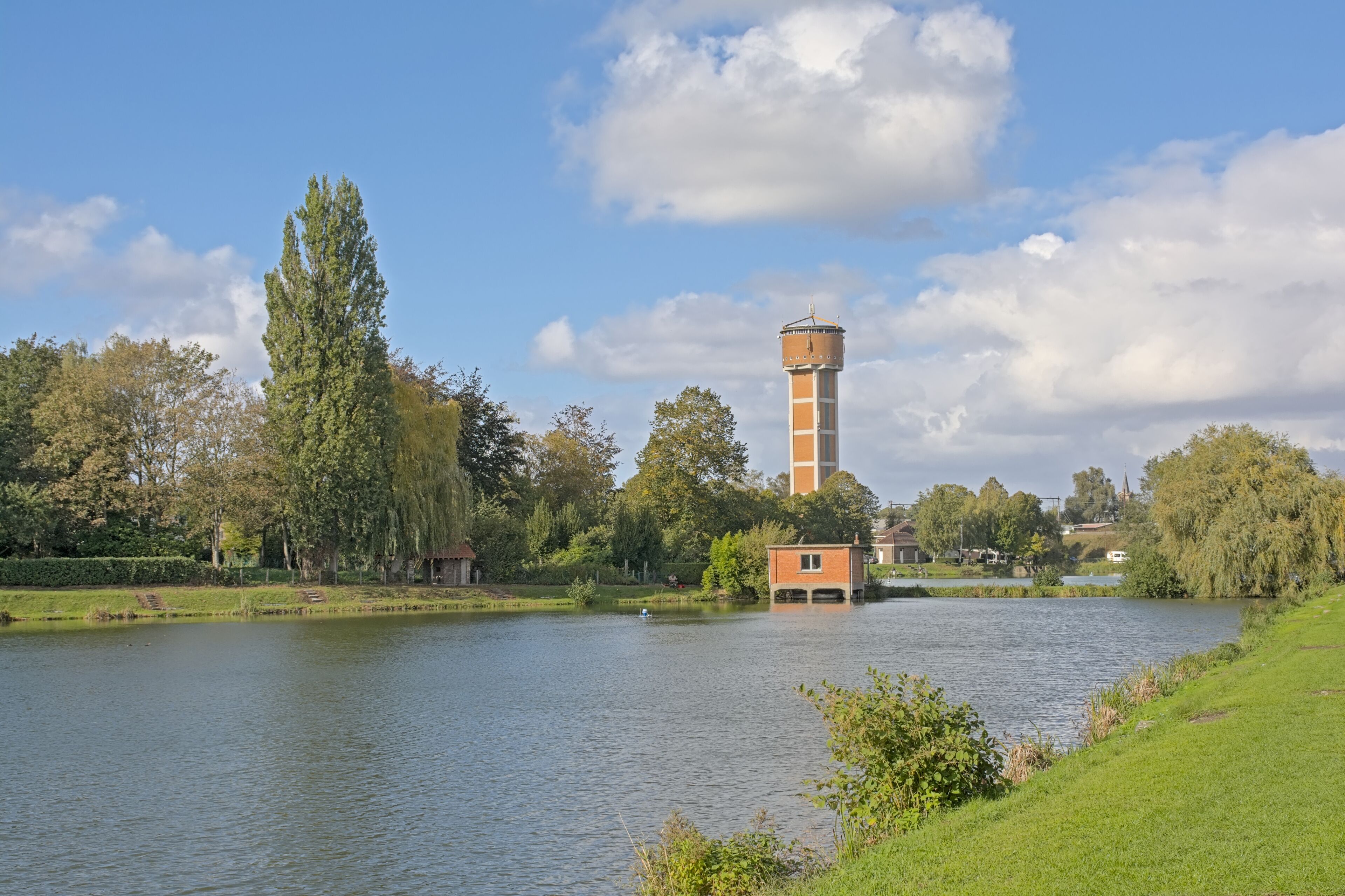 A calm lake with a tower and a small building on the shore.