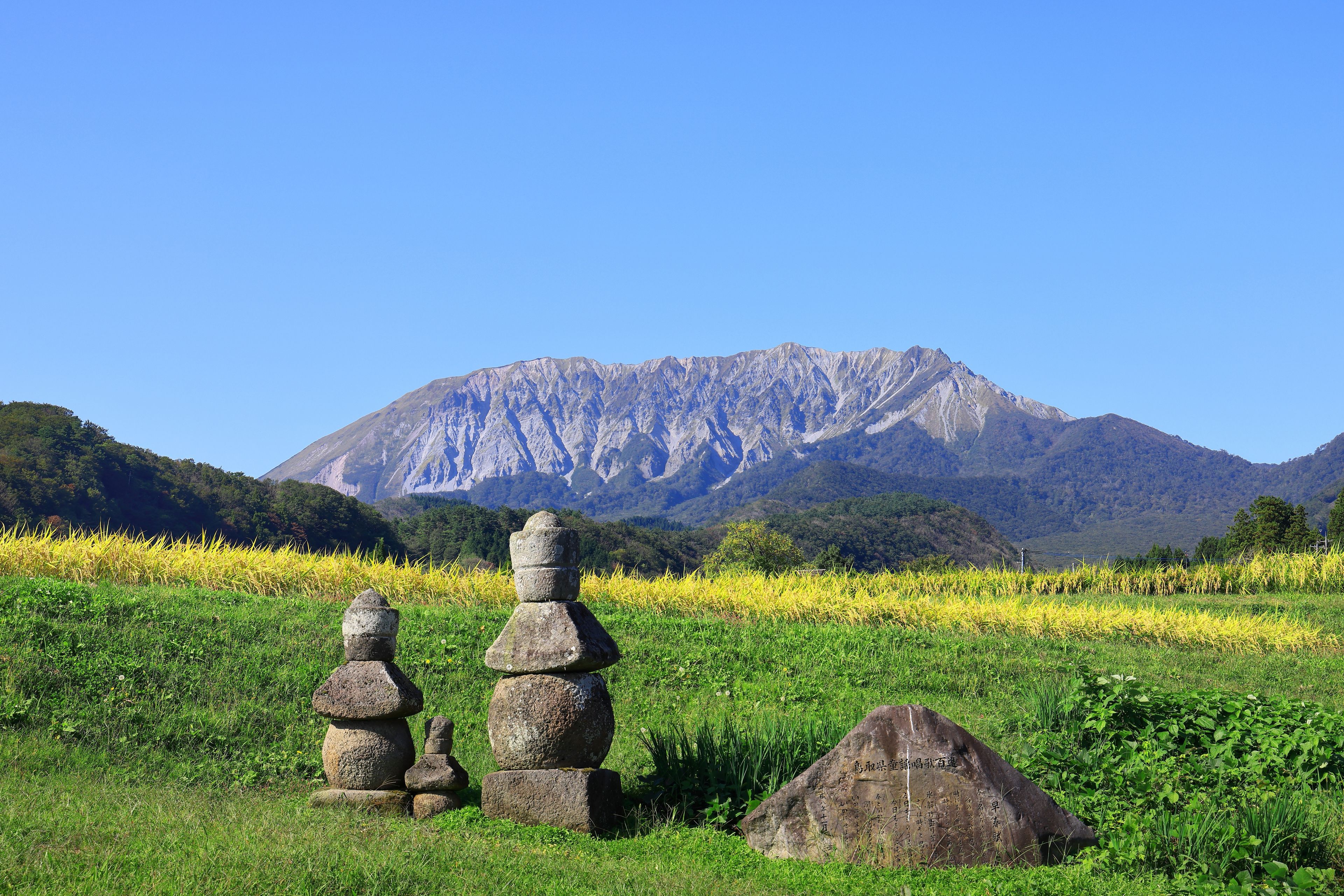Ein Steinmonument in einer grünen Wiese mit einem Berg im Hintergrund.