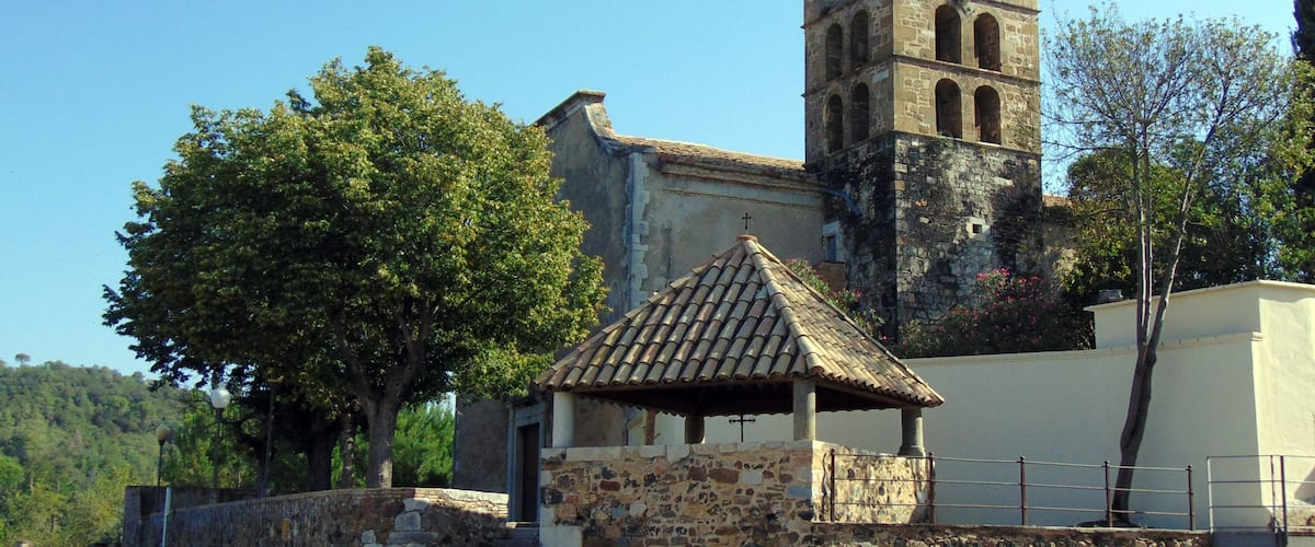 Una iglesia con un campanario, paredes de piedra y un pequeño pabellón.