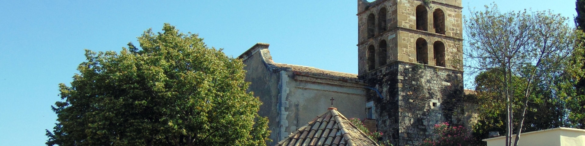 Una iglesia con un campanario, paredes de piedra y un pequeño pabellón.