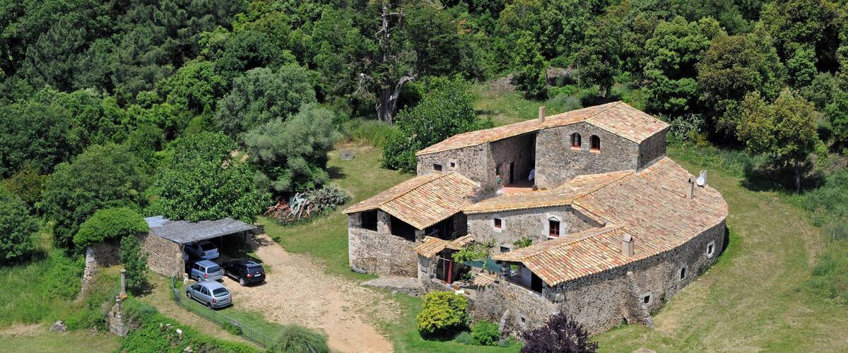 A stone house with a tiled roof surrounded by lush greenery and a swimming pool.