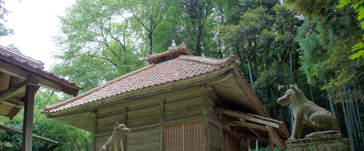 A traditional wooden structure with a tiled roof, surrounded by lush greenery and stone statues.