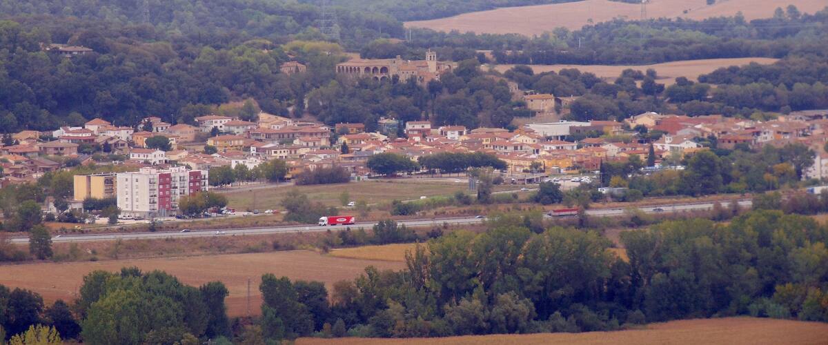 A town with a mix of residential and commercial buildings, surrounded by fields and hills.