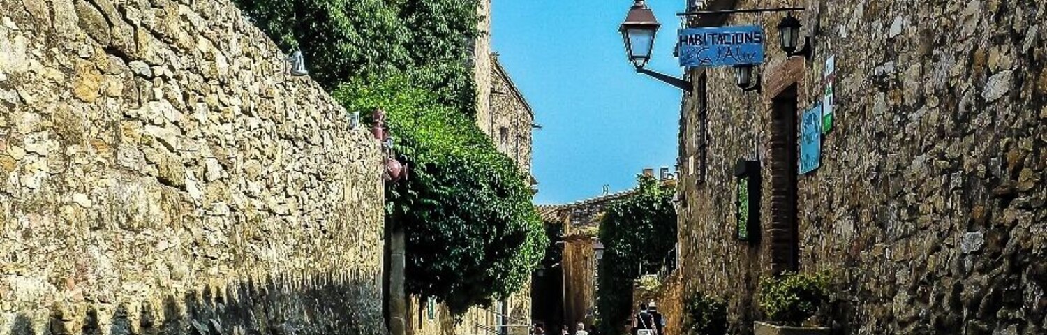 A narrow cobblestone street flanked by stone buildings, a stone tower, and a sign for 'Habitations'.