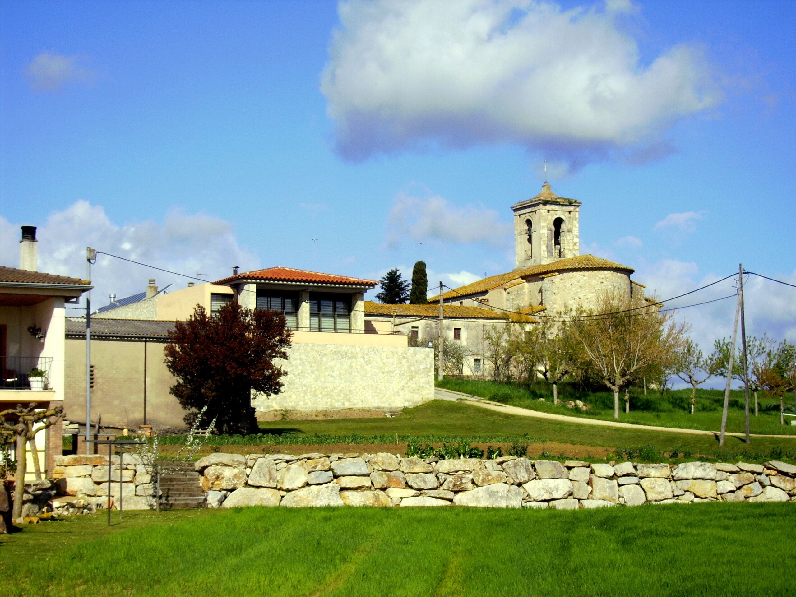A stone church with a bell tower, surrounded by a stone wall and a grassy area.