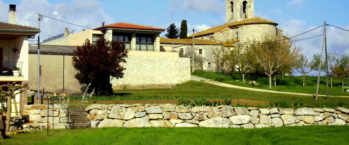 A stone church with a bell tower, surrounded by a stone wall and a grassy area.