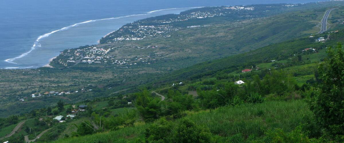 A coastal landscape with a winding road, green hills, and a beach.