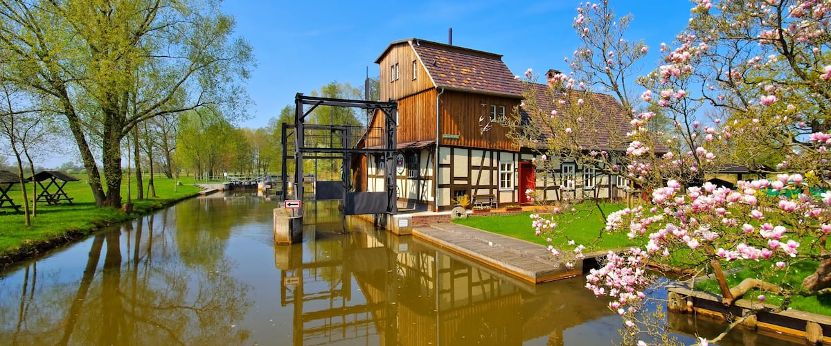 A canal with a traditional wooden house and blooming trees.