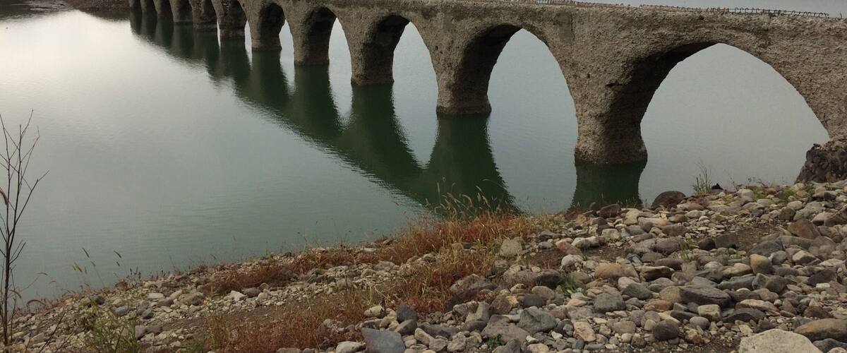 A stone bridge over a calm lake with mountains in the background.