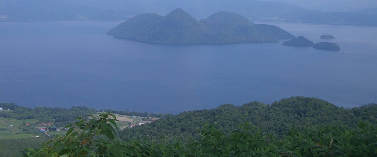 A coastal landscape with a large body of water, several islands, and a distant shoreline with greenery and buildings.