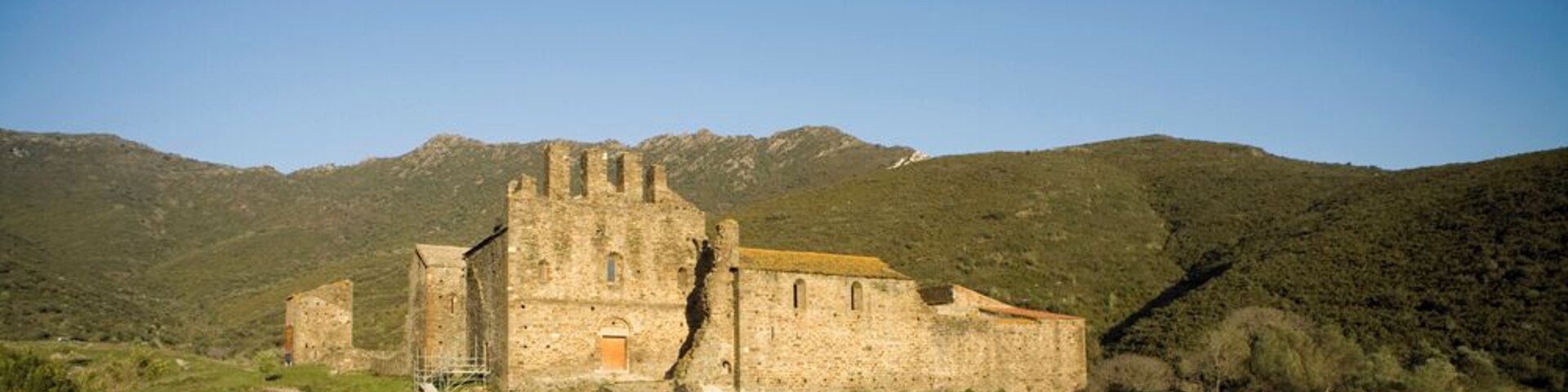 Un castillo de piedra antiguo con una torre destacada, rodeado de colinas verdes y un cielo despejado.