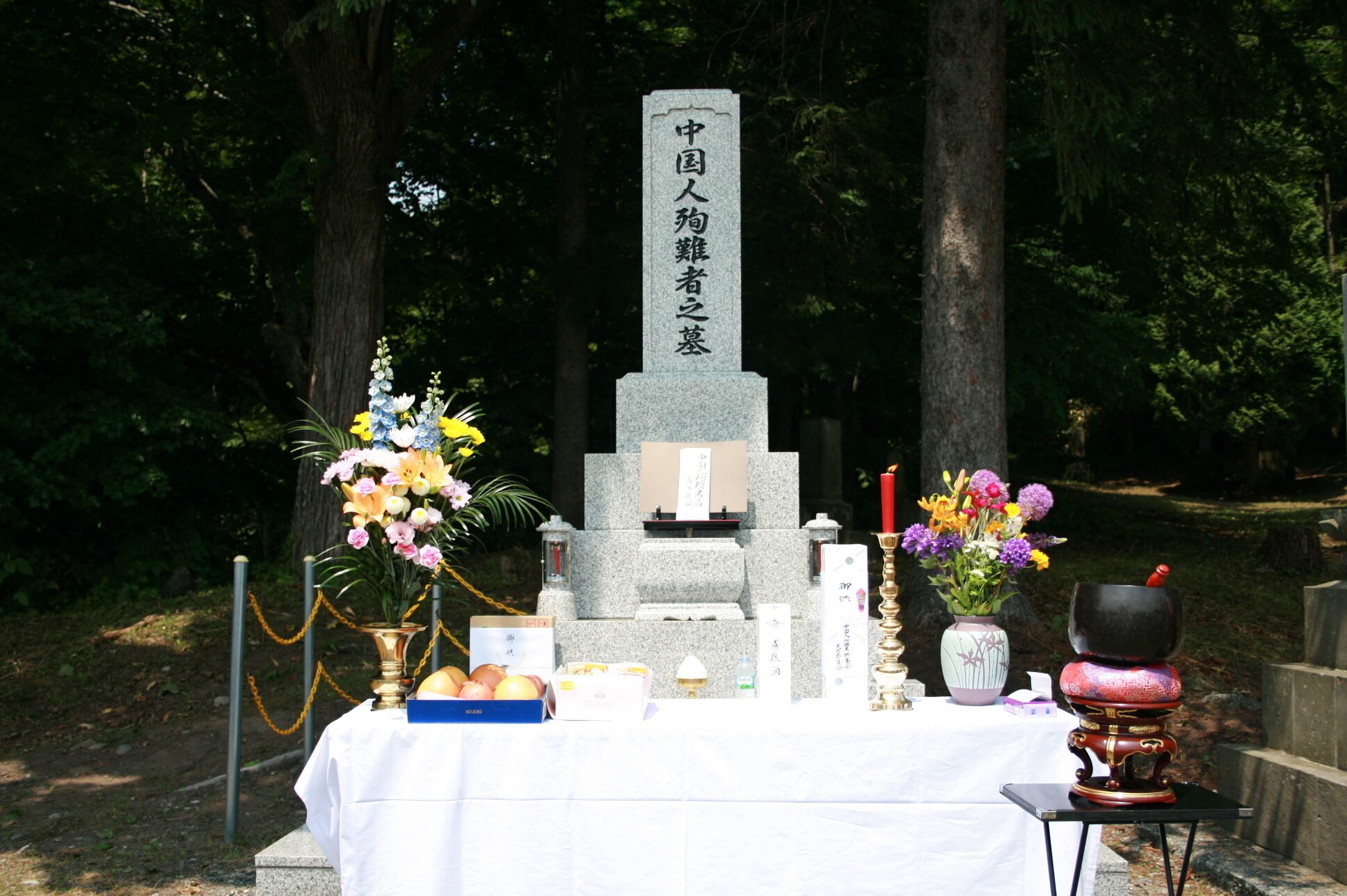 A memorial with a stone monument, flowers, and offerings.