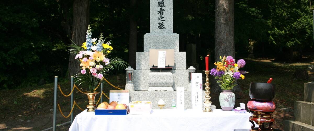 A memorial with a stone monument, flowers, and offerings.