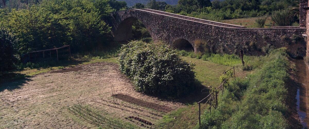 A stone bridge over a river, surrounded by lush greenery and mountains in the background.