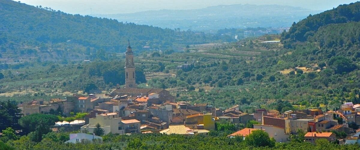 A town nestled in a valley with a prominent tower, surrounded by lush greenery and rolling hills.
