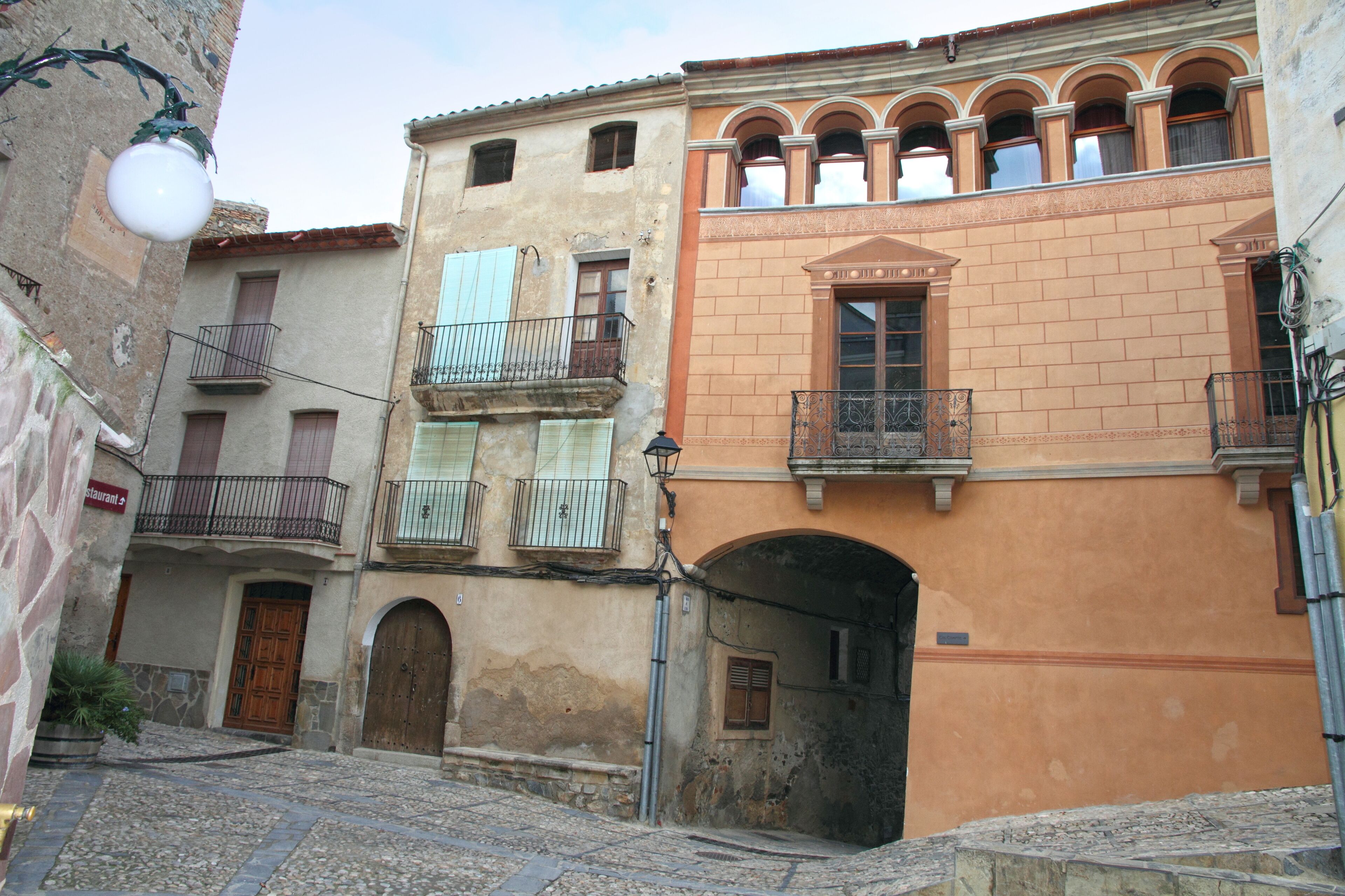 A narrow cobblestone street with historic buildings, a wooden door, and a street lamp.