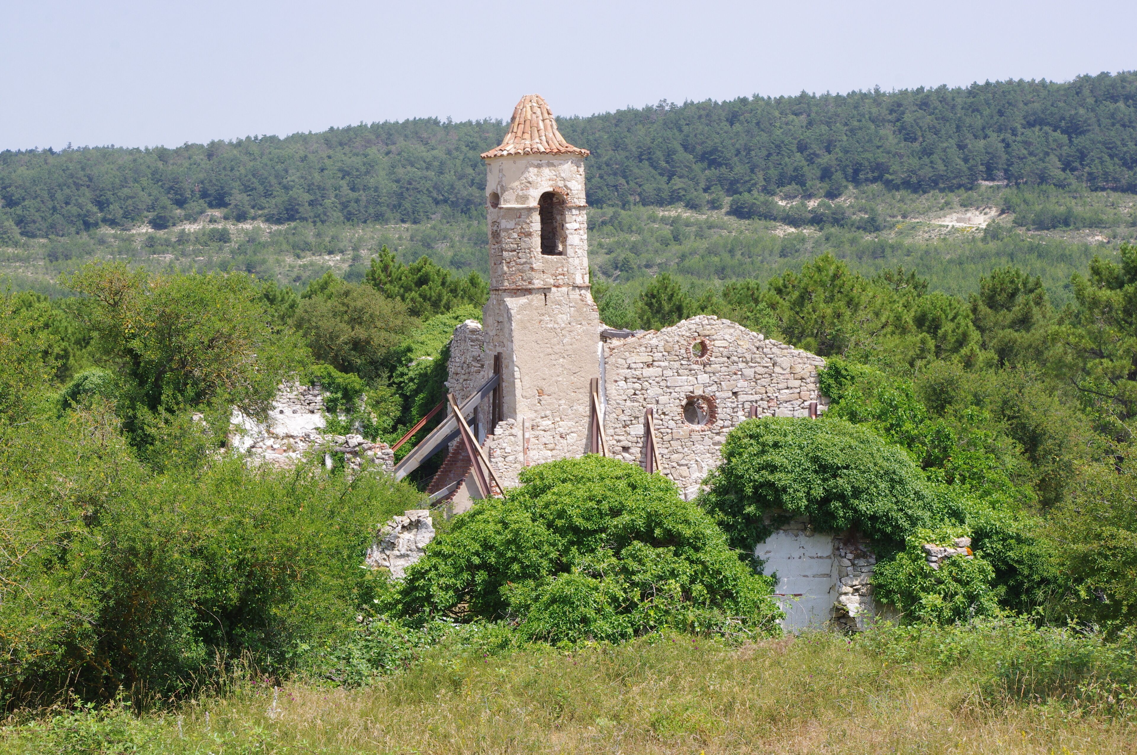 An ancient stone tower surrounded by lush greenery and forested hills.
