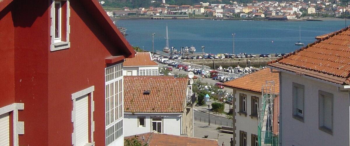 A coastal town with red-roofed buildings, a marina, and hills in the background.