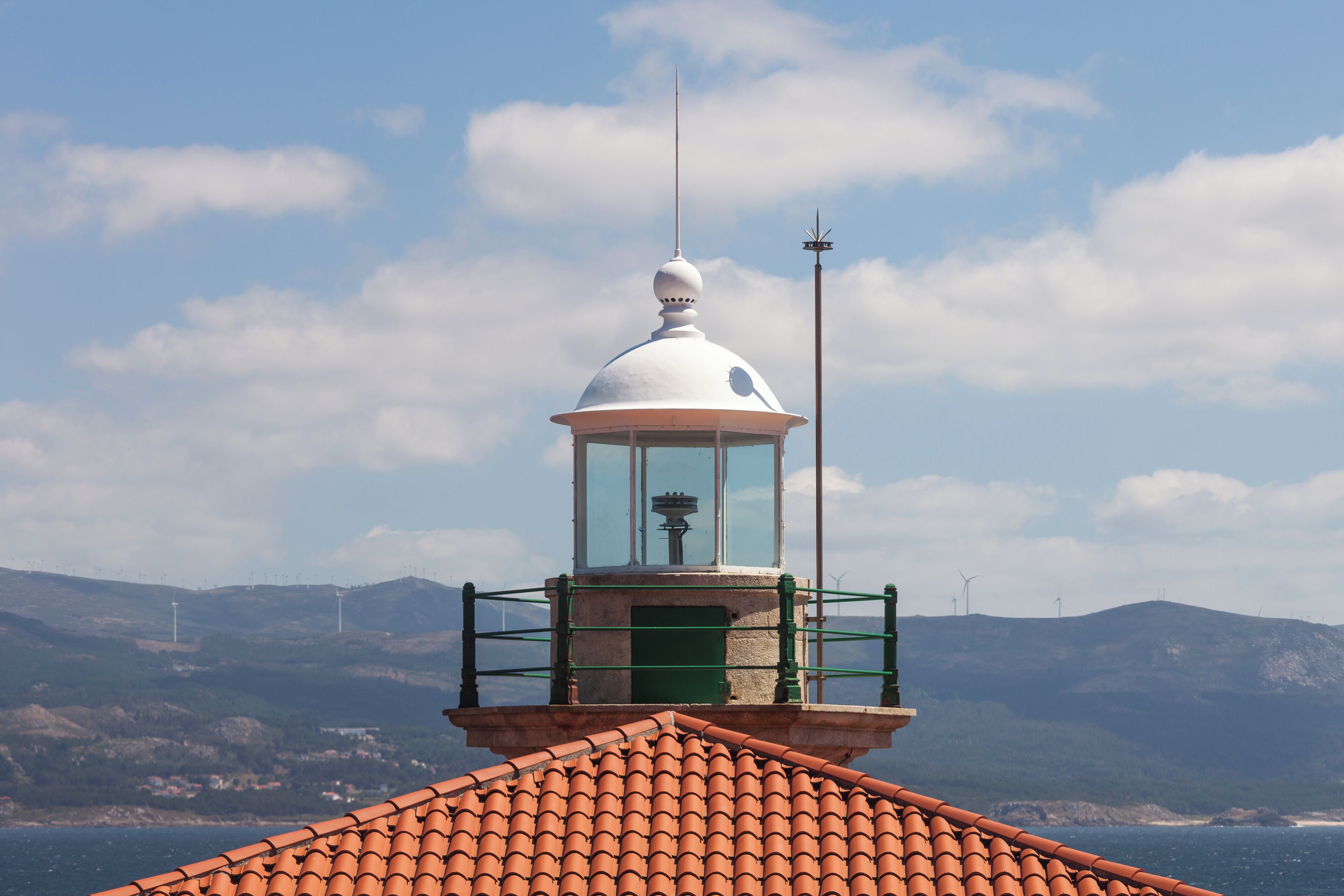 A lighthouse with a red-tiled roof, a white dome, and a green railing.