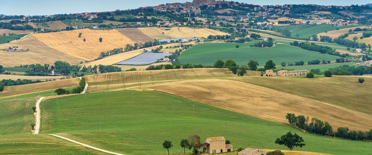 A rural landscape with rolling hills, fields, and a distant town with a prominent castle-like structure.
