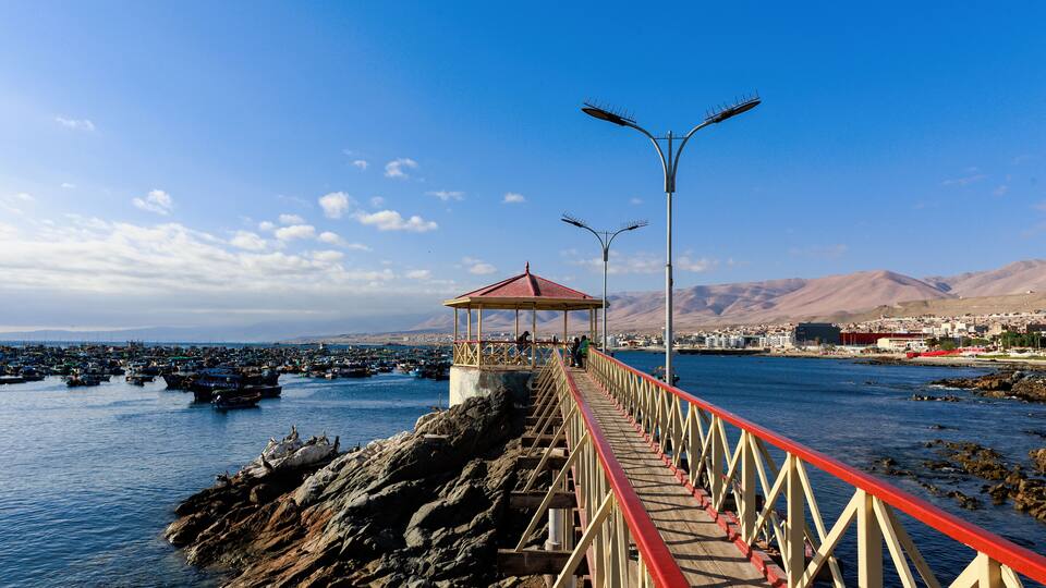 A pier with a red railing leading to a gazebo by the water.