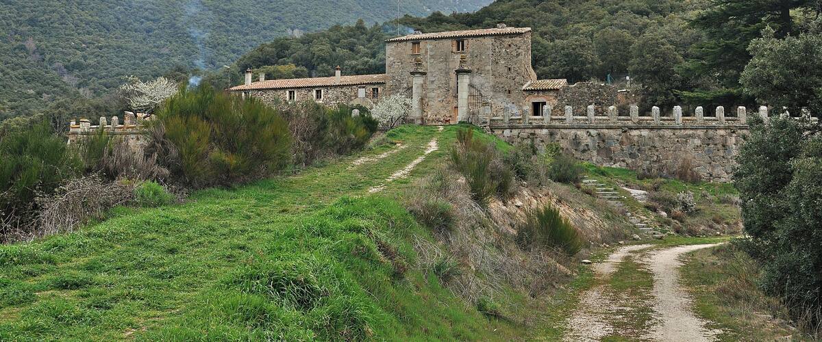 A stone building with a tiled roof surrounded by a stone wall and a path leading to it.