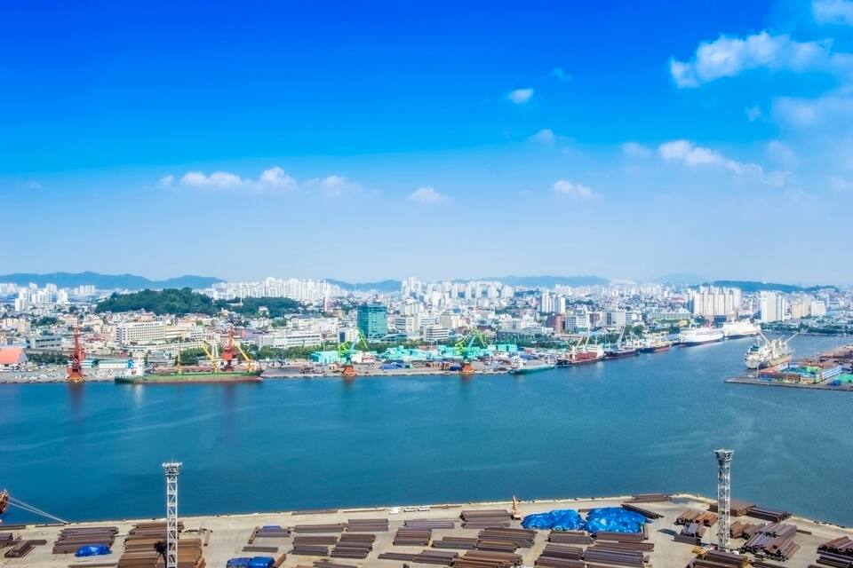 Eine Küstenlandschaft mit Fluss, Industriekranen und einem Kreuzfahrtschiff, das im Hafen liegt.