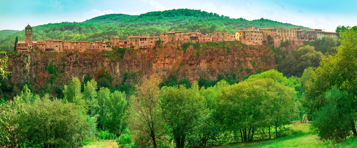 A historic town perched on a cliff with lush greenery and a prominent tower.