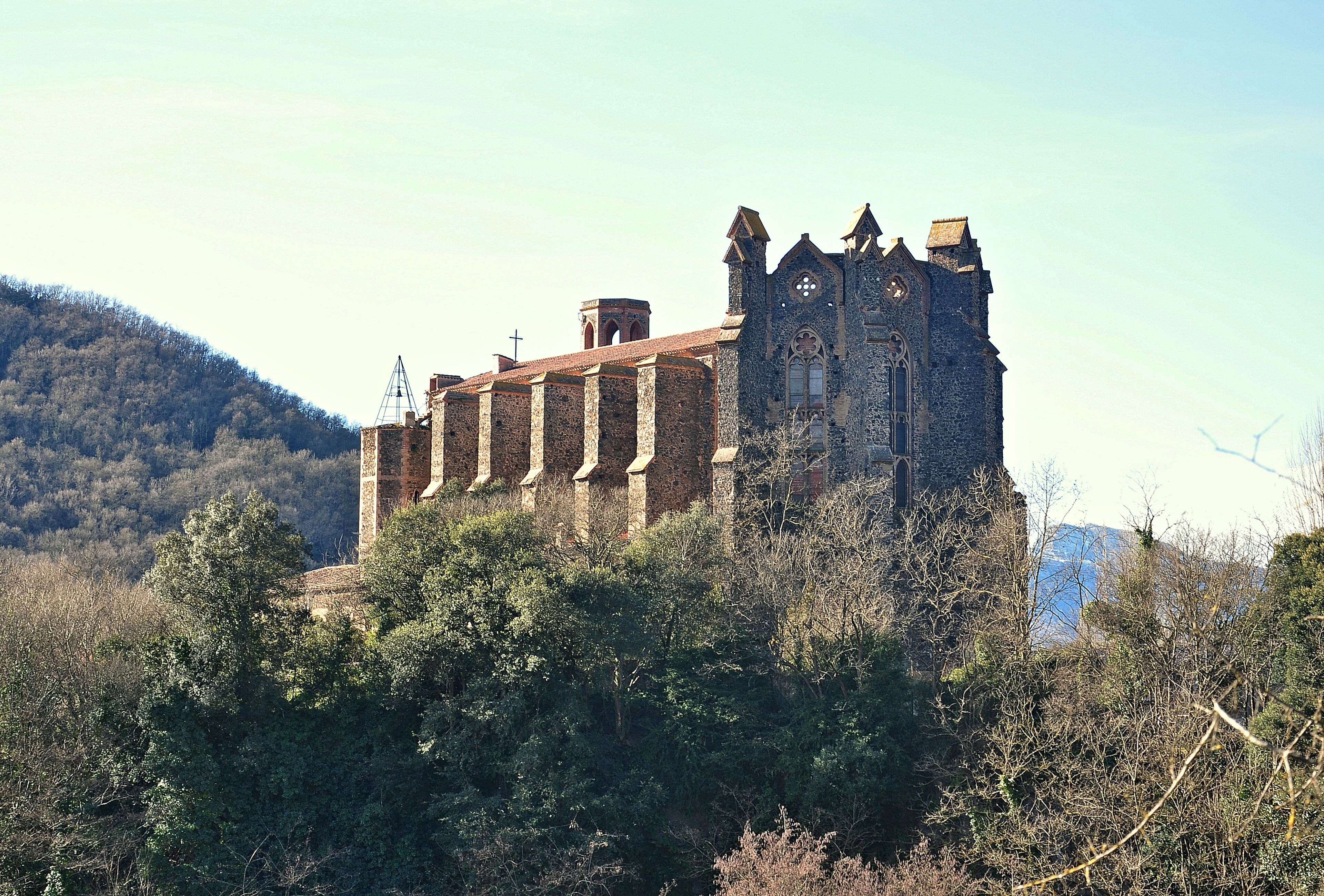 A historic stone building with a tower, surrounded by dense forest and hills.